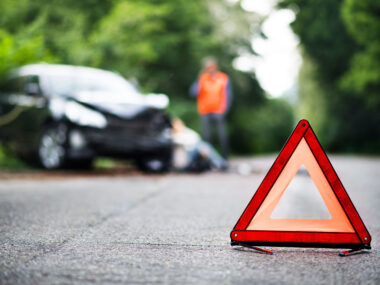 A close up of a red emergency triangle on the road in front of a car after an accident.