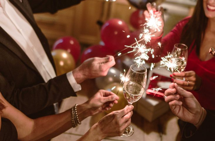 Feiernde stoßen mit einem Glas Sekt und Sprühkerzen auf das neue Jahr an.