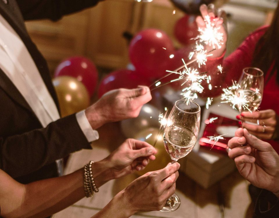 Feiernde stoßen mit einem Glas Sekt und Sprühkerzen auf das neue Jahr an.
