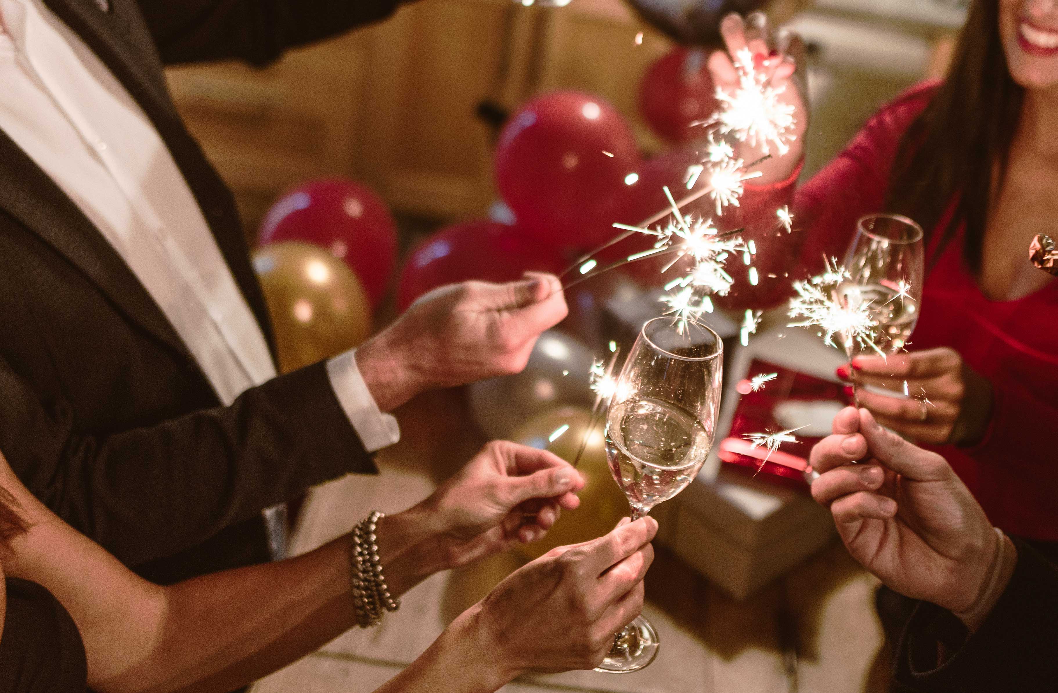 iStock/Franckreporter Feiernde stoßen mit einem Glas Sekt und Sprühkerzen auf das neue Jahr an.