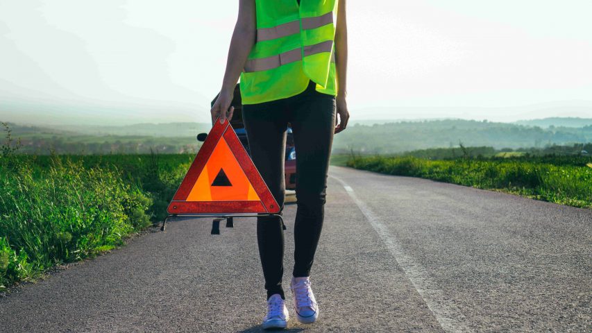 Frau mit Warnweste leistet Erste Hilfe im Straßenverkehr