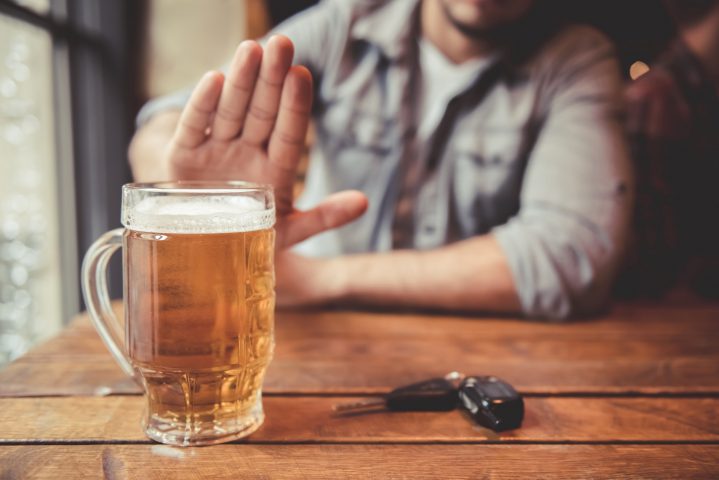 Das Bild zeigt einen Mann, der an einem Tisch sitzt und eine ablehnende Geste Richtung eines vollen Bierglases macht. Vor ihm liegt ein Autoschlüssel.