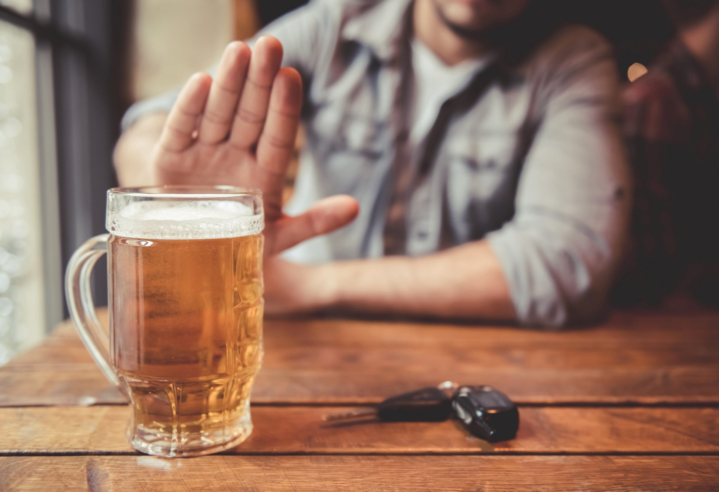 iStock/GeorgeRudy Das Bild zeigt einen Mann, der an einem Tisch sitzt und eine ablehnende Geste Richtung eines vollen Bierglases macht. Vor ihm liegt ein Autoschlüssel.
