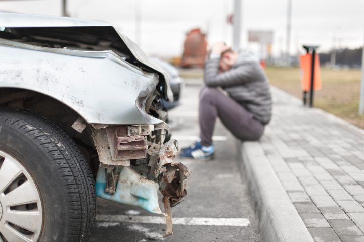 Ein Mann sitzt neben einem verunfalltem Fahrzeug