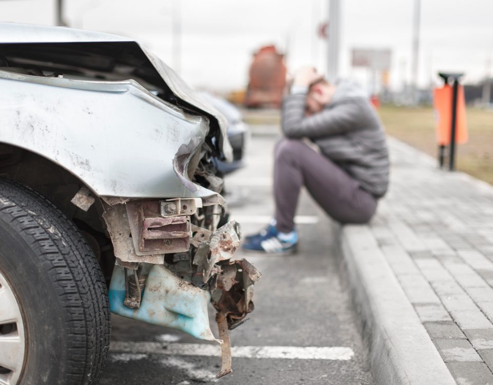 Ein Mann sitzt neben einem verunfalltem Fahrzeug