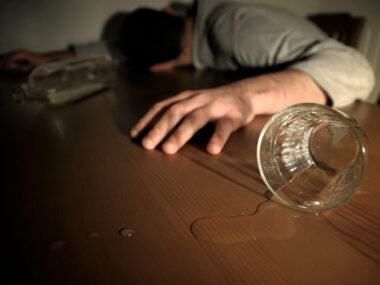 Mann ohne Bewusstsein neben einer leeren Flasche