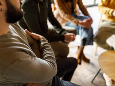 Man sitting with arms crossed, listening to people sharing their stories during a group therapy session